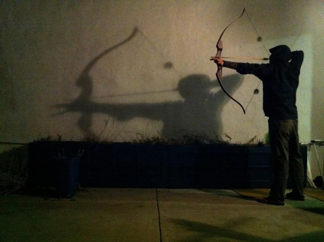 Nute drawing a bow, his shadow cast on the wall